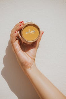 A close-up of a hand holding a skincare product with a minimalist design against a neutral background.