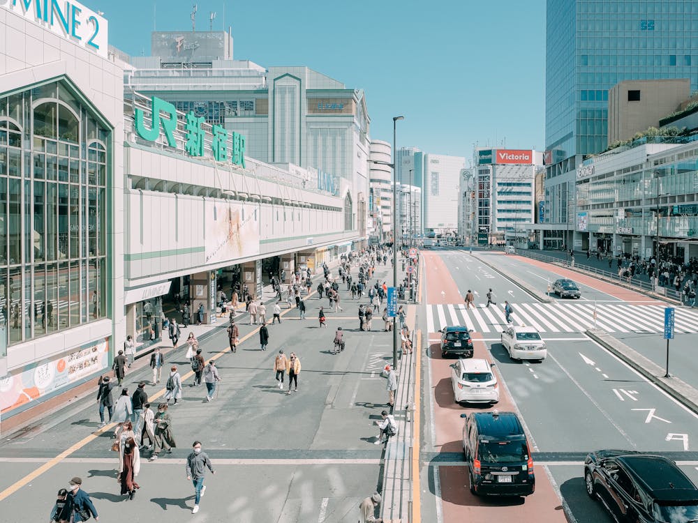 From above of unrecognizable people walking near road and modern Shinjuku Station located against cloudless blue sky in Tokyo