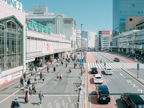 Free From above of unrecognizable people walking near road and modern Shinjuku Station located against cloudless blue sky in Tokyo Stock Photo