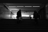 Back view black and white of anonymous passengers walking up staircase leaving subway station