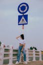 Woman in White Crop Top and Denim Jeans Leaning on a Street Sign