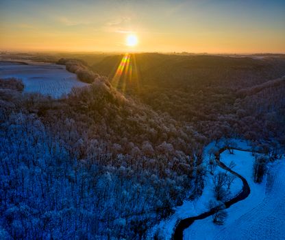 Scenic winter landscape with sun rays over Minnesota's snowy river valley captured from above.