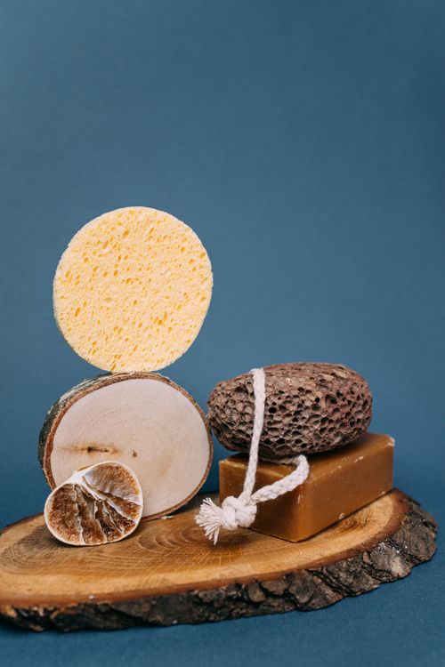 Free A collection of spa essentials including sponge, soap, and pumice stone on a wooden stand against a blue background. Stock Photo