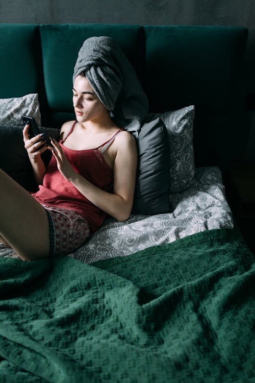 Free Woman Sitting on the Bed While Using Her Smartphone  Stock Photo