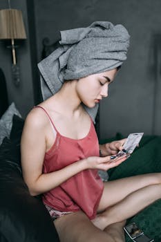 A woman in casual attire enjoys a skincare moment indoors with natural light.