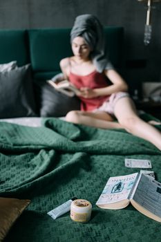 Woman in bedroom reading a book, surrounded by skincare products. Cozy and serene atmosphere.