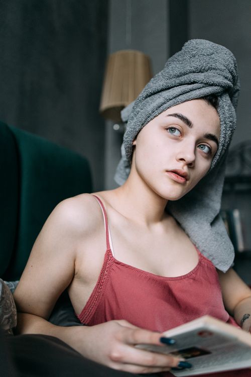 Free Young woman with towel on head reading a book indoors, exuding calm and relaxation. Stock Photo
