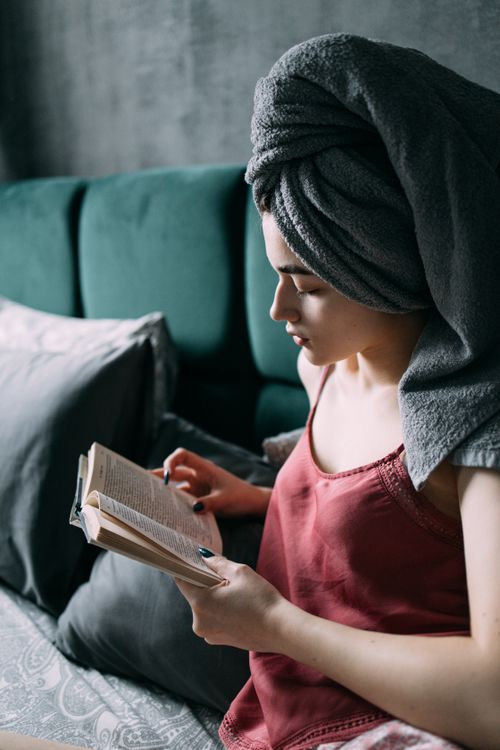 Free A woman with a towel on her head reads a book in a comfortable bedroom environment. Stock Photo