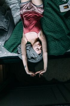 Young woman in pink attire relaxing on a bed with arms raised in the bedroom.