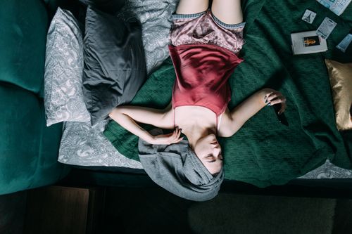 Free Young woman in a relaxing bedroom setting using a smartphone with a towel on her head. Stock Photo