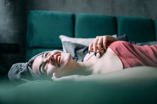 Young woman with towel on head smiles while relaxing indoors.