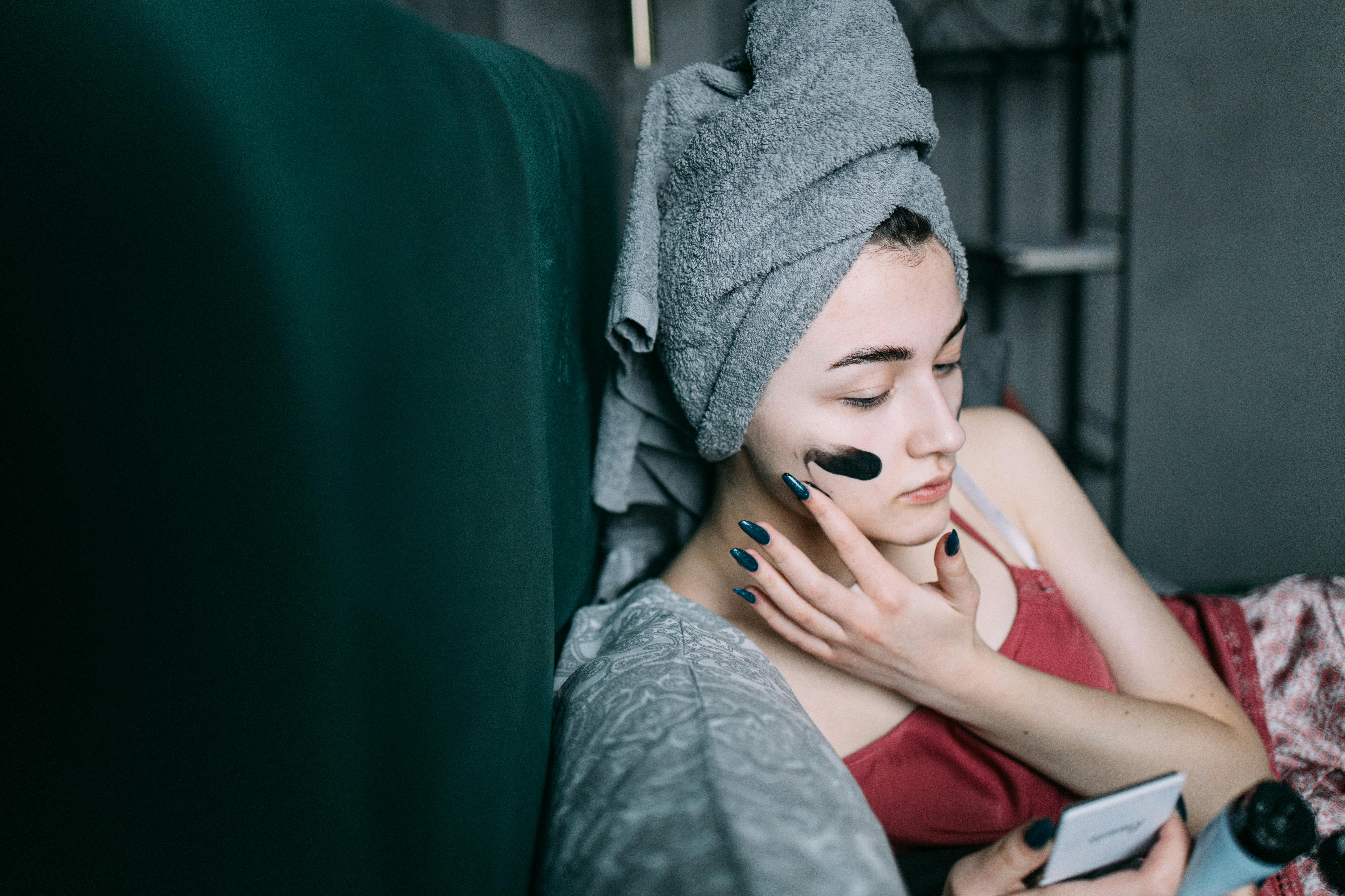 Woman at home applying a facial mask for relaxation and skincare. Self-care routine with a towel on head.