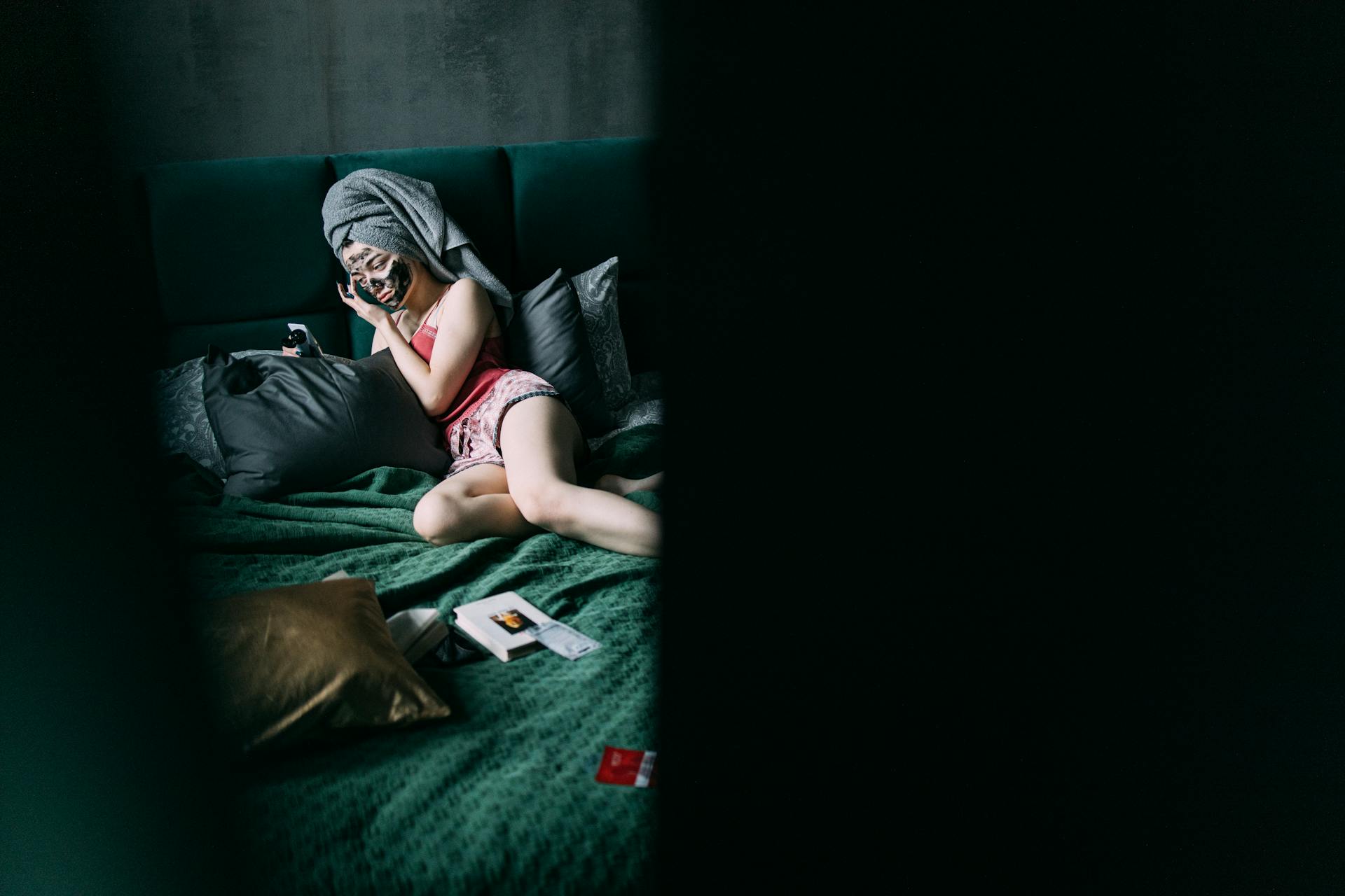 Woman Lying on Bed with Charcoal Facial Mask on Her Face