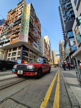 Vibrant cityscape featuring a red taxi on a bustling street, surrounded by tall buildings.