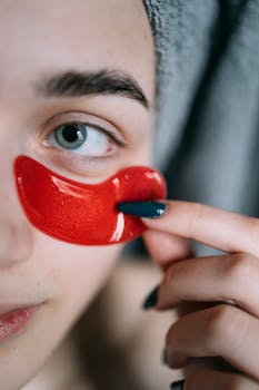 Extreme close-up of a woman applying a red eye patch for skincare and rejuvenation.
