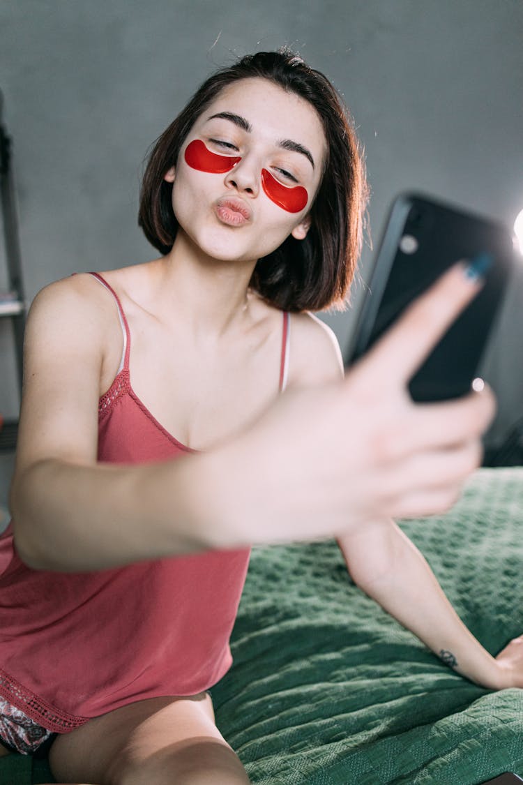 A Woman With An Under Eye Patches Taking A Selfie