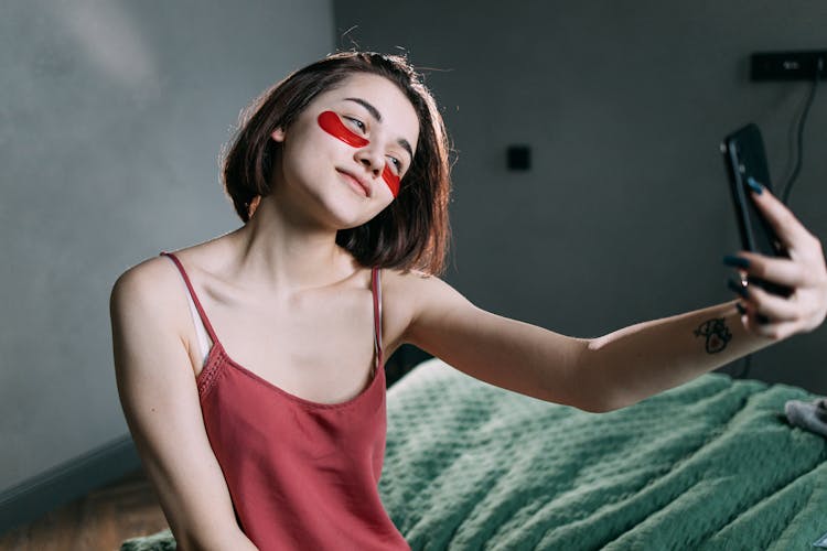 A Woman With An Under Eye Patches Taking A Selfie