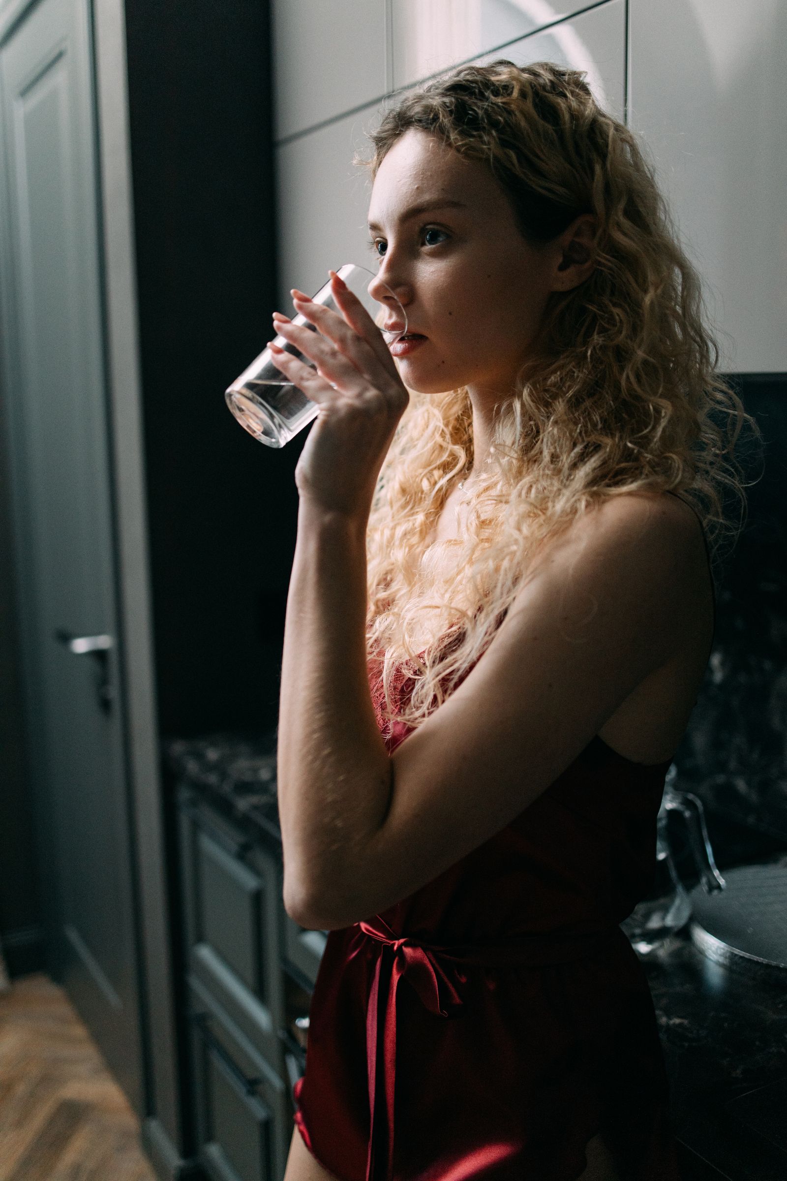 A woman drinking a glass of water in her kitchen, the habit with the strongest trial evidence for fewer recurrent UTIs