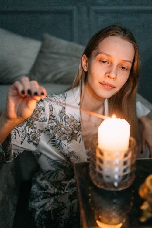 Free A woman in pajamas lights a candle, creating a peaceful and intimate atmosphere indoors. Stock Photo