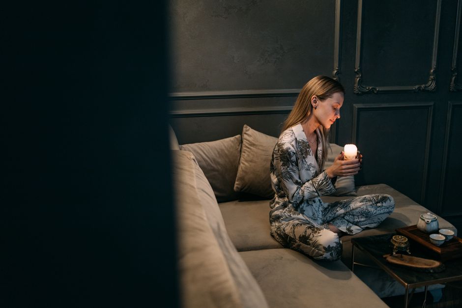 Mulher de pijama segurando uma vela, sentada em um sofá aconchegante em um ambiente sereno