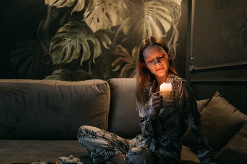Free A woman in pajamas holding a candle while sitting on a sofa, creating a cozy indoor atmosphere. Stock Photo