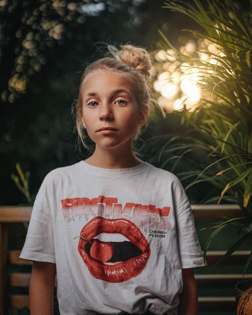 Free A young girl with blonde hair in a white shirt poses outdoors at sunset. Stock Photo