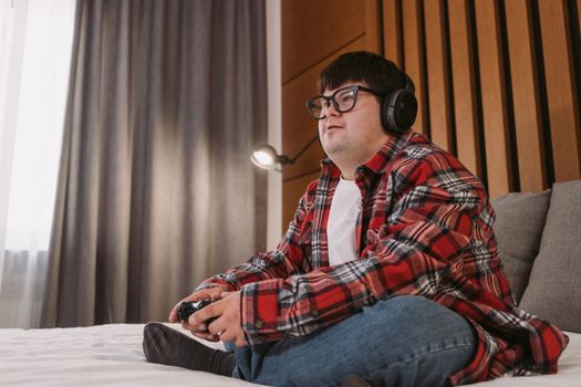 Young man with headphones playing video games on a bed, enjoying leisure time indoors.