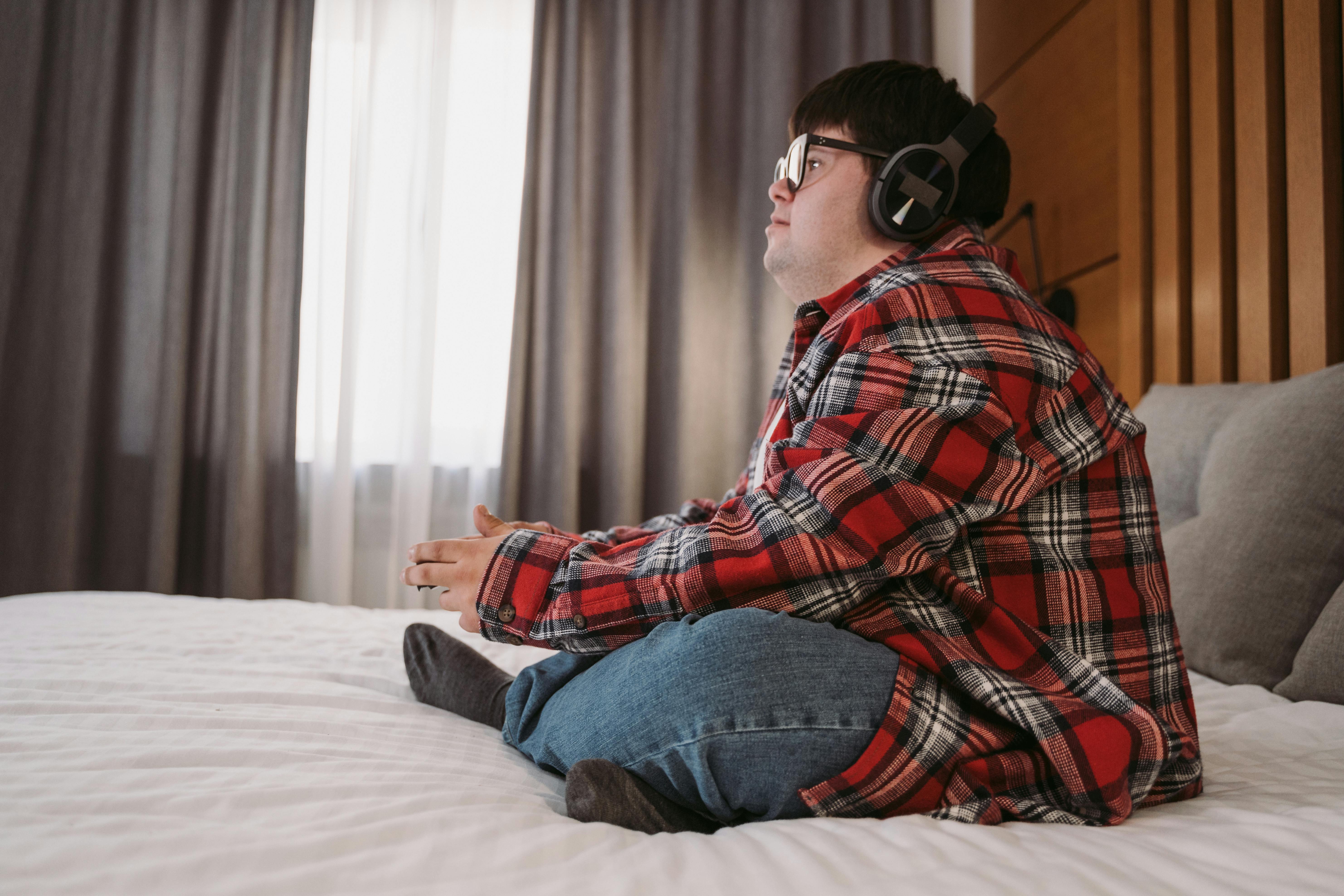 man in red white and black plaid dress shirt and blue denim jeans sitting on bed