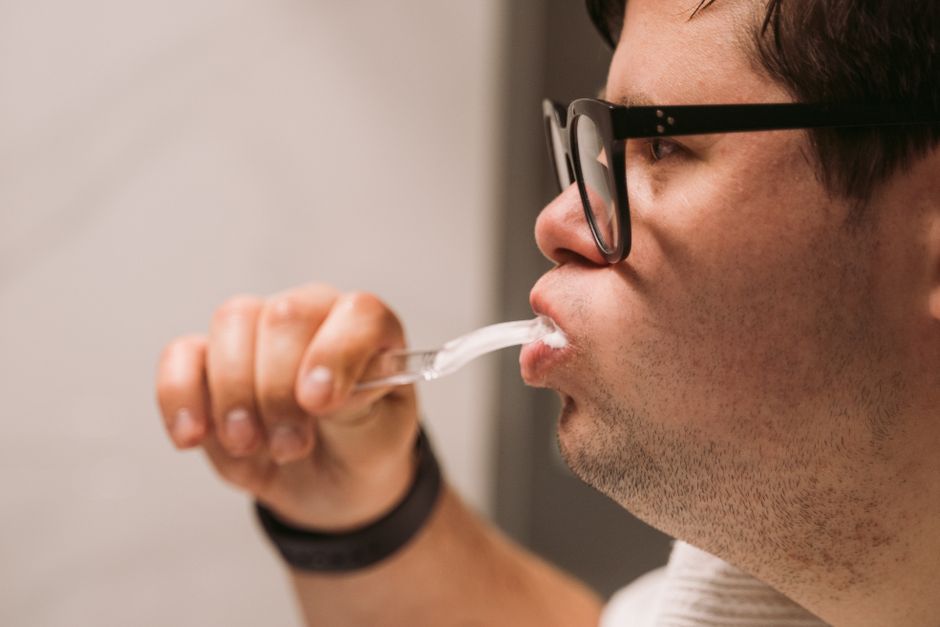 oral pH balance - Side view of a man with glasses practicing oral hygiene by brushing teeth indoors.