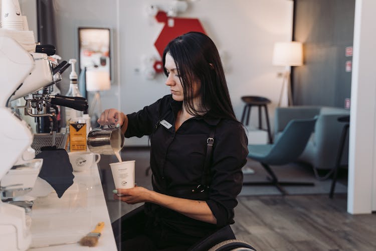 A Woman In Black Long Sleeves Pouring Milk On A Paper Cup