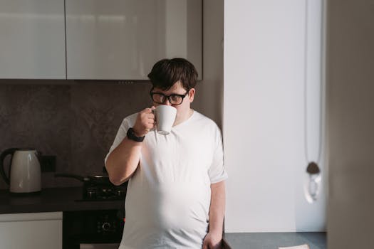 Man with eyeglasses sipping coffee in a modern kitchen setting.