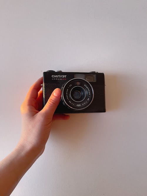 Crop hand of woman holding 35 mm analog photo camera against white wall