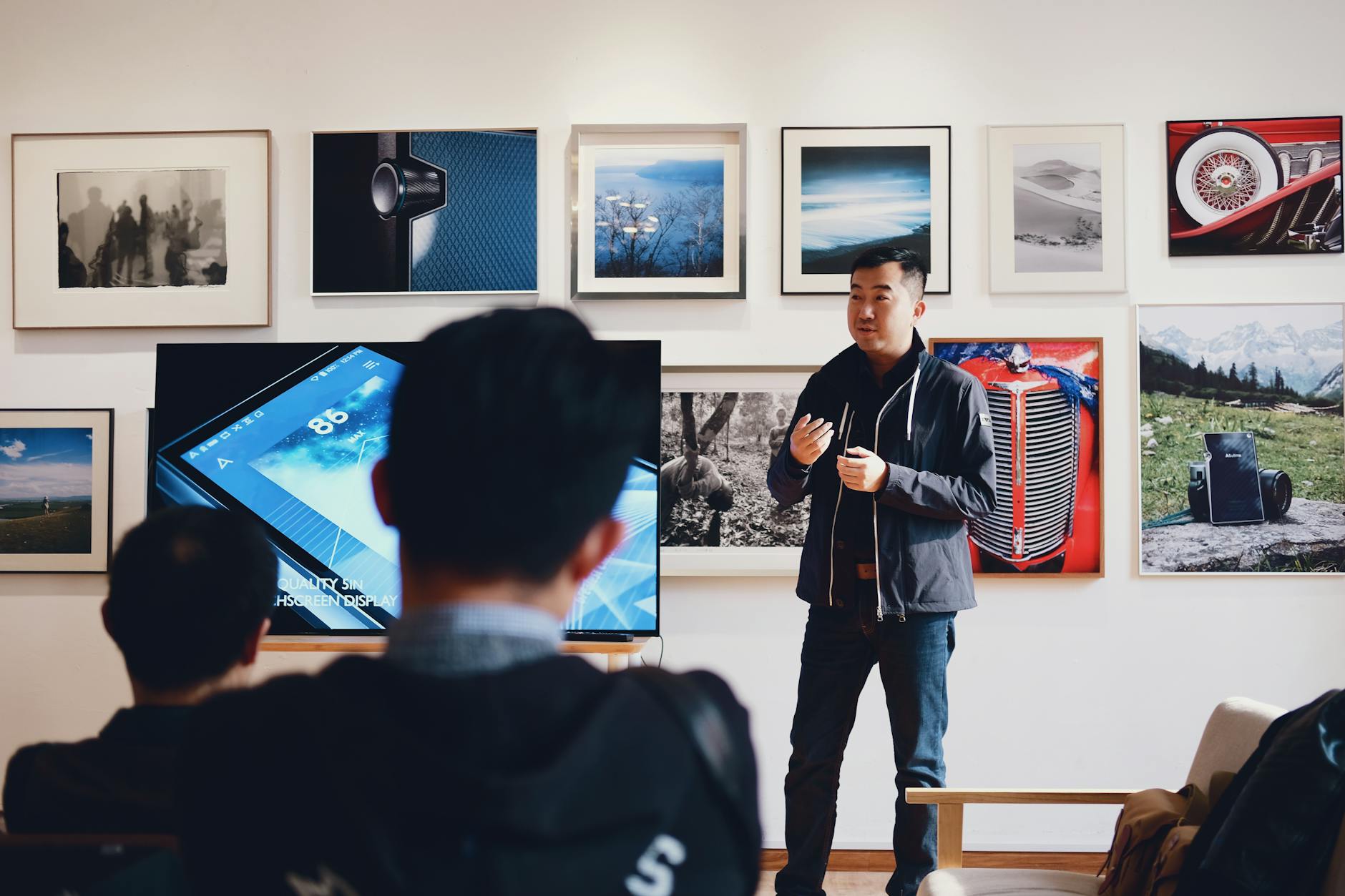 A MAN TALKING TO TWO PEOPLE BESIDE A FLAT SCREEN WITH PHOTOS IN THE BACKGROUND 