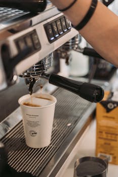 A barista brews fresh coffee into a paper cup using an espresso machine.