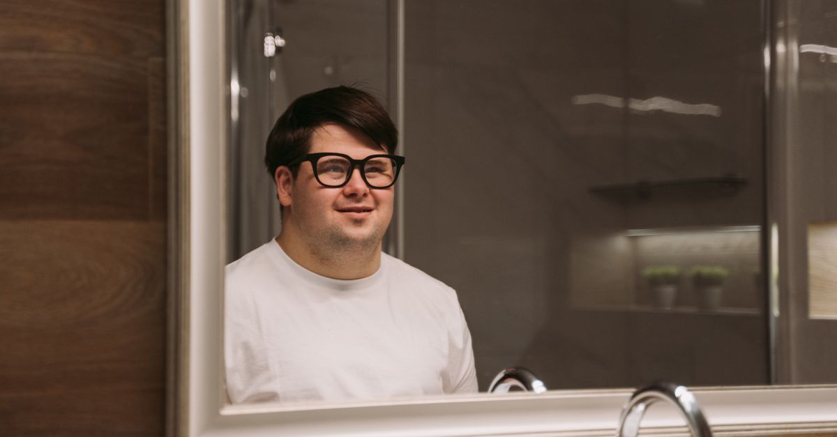 A man smiles at his own reflection in a bathroom mirror.