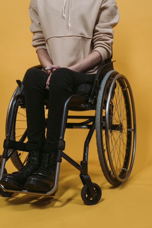 Free A person sitting in a wheelchair wearing black boots and a hoodie, set against a bright yellow backdrop. Stock Photo