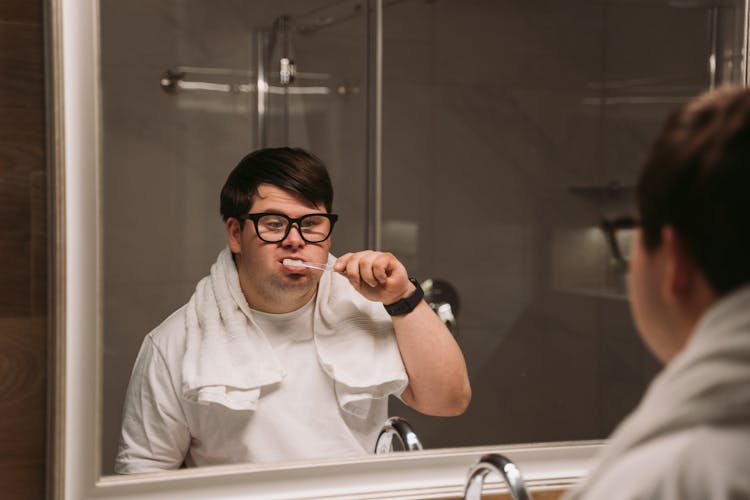 A Man In White Shirt Looking At The Mirror While Brushing His Teeth