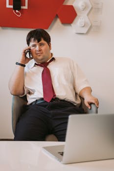 A man in a shirt and tie talks on his cellphone while seated in an office setting.