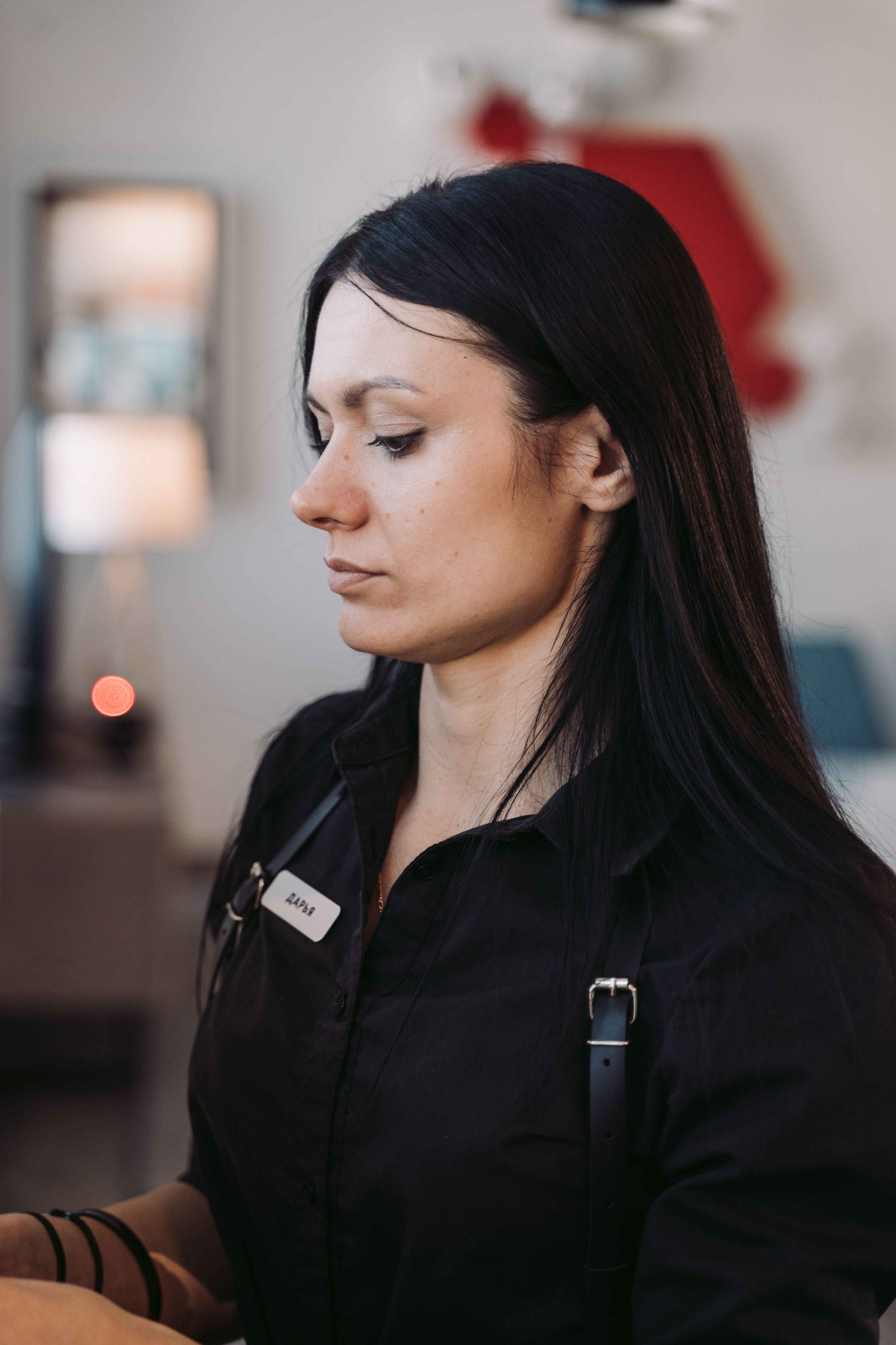 Profile portrait of a woman with long black hair wearing black clothing, standing indoors.