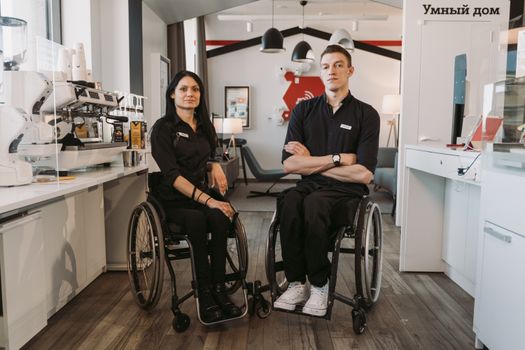 Two baristas in wheelchairs at a modern coffee shop, emphasizing accessibility.