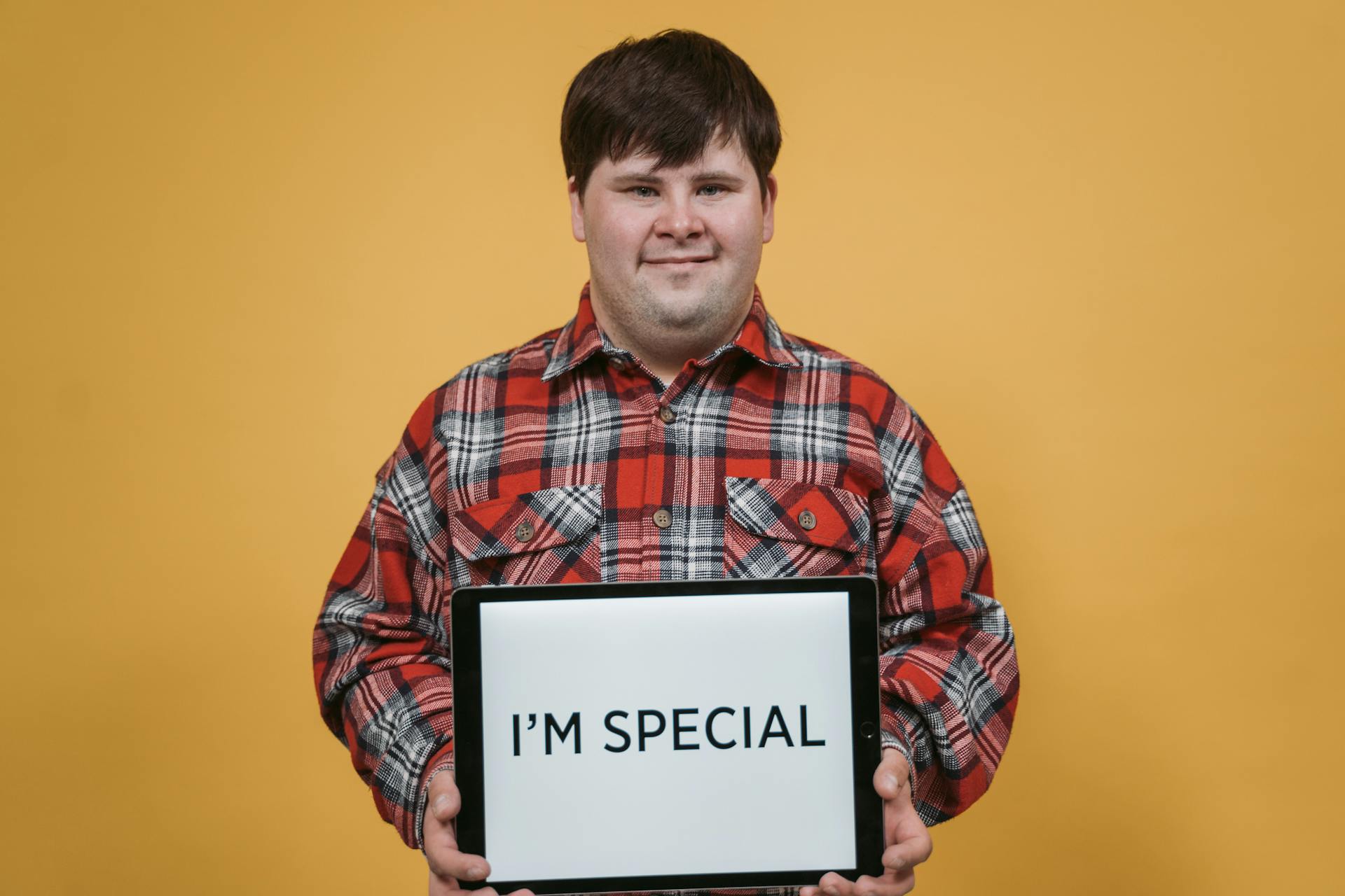 Man Holding an Ipad with a Message on a Yellow Background