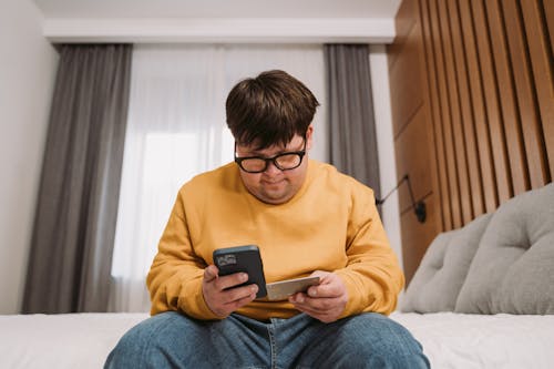 Free Man in Yellow Sweater Holding Black Smartphone and Credit Card Stock Photo