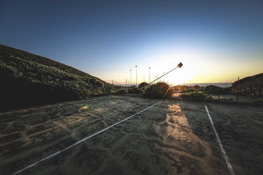 A sunset view of an abandoned sports court with cracked surface and slanted floodlights.