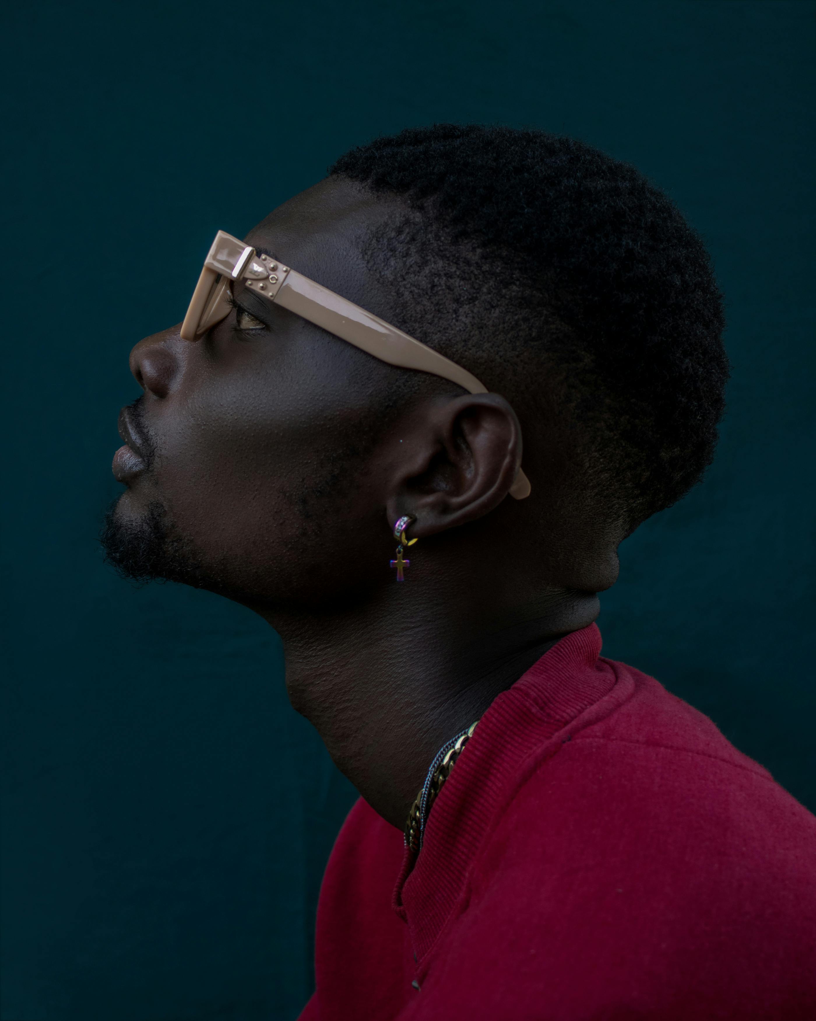 Close-up of a fashionable man in sunglasses and jewelry, showcasing modern style in a studio setting.