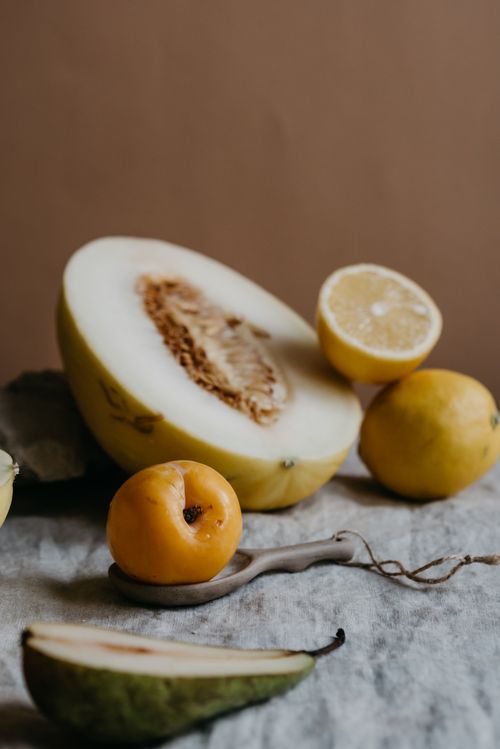 Free Artistic arrangement of fresh melon, lemon, and pears on linen backdrop in studio lighting. Stock Photo