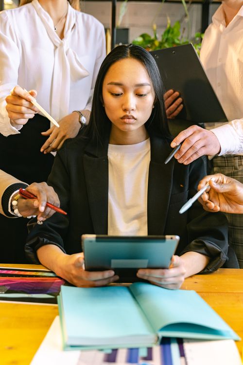 Free Focused young professional woman using a tablet amidst a busy office environment. Stock Photo