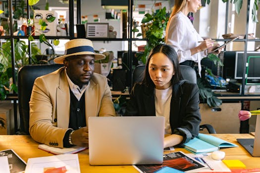 Professional team collaborating at a desk with laptops, tablets, and documents in a vibrant office space.