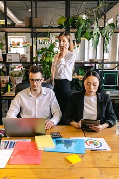 Three diverse colleagues working in a bright, modern office with technology and documents, enhancing productivity.
