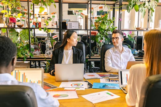 A diverse team of professionals discussing projects in a plant-filled office setting.