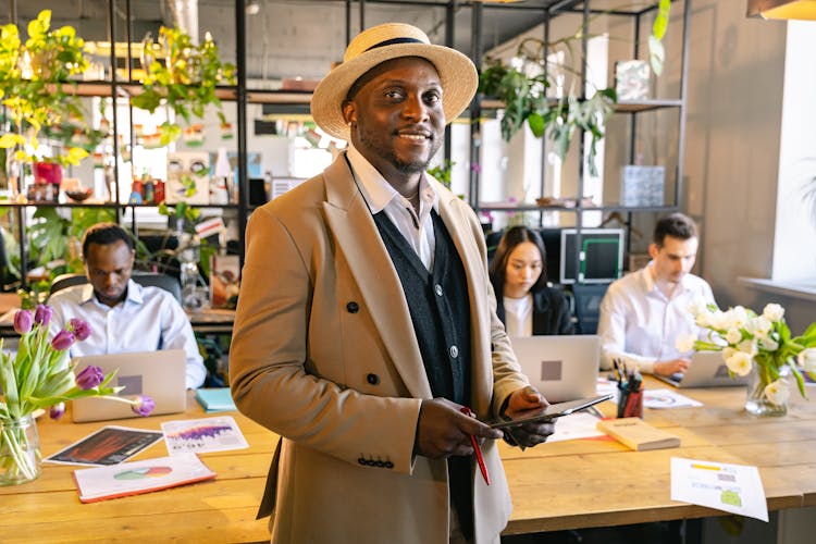 A Man In Beige Suit Smiling While Holding A Tablet